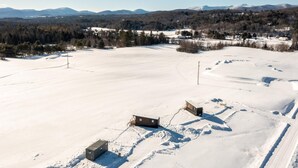 Paisagem coberta de neve com duas cabanas e vista clara para montanhas distantes.