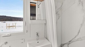 Casa de banho com lavatório branco, espelho e vista para uma paisagem nevada.