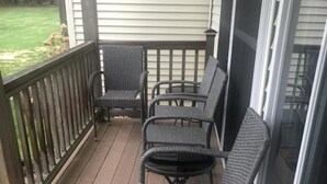 Un portico coperto con quattro sedie in vimini e un tavolino, pavimento in legno decking e vista su un prato.