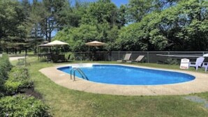 Una piscina circondata da erba e alberi, con lettini e ombrelloni.