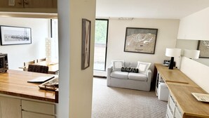 Eine moderne Küche mit Holzausstattung, einem Esstisch und einer Kücheninsel. Im Wohnbereich befindet sich ein graues Sofa mit einem Kissen mit dem Aufdruck 'Vermont' und eine gerahmte Karte an der Wand.