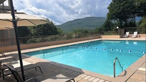 Ein rechteckiger Swimmingpool mit klarem, blauem Wasser, umgeben von einer gefliesten Liegefläche mit Liegestühlen und Sonnenschirmen.