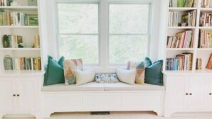 A room with a built-in bench under a window, surrounded by bookshelves filled with books. - Serene & Cozy 3BR Home w/ Large Deck on River (Stowe)