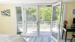 A bedroom with a bed, a desk with a lamp, and a sliding glass door leading to a balcony. - Serene & Cozy 3BR Home w/ Large Deck on River (Stowe)