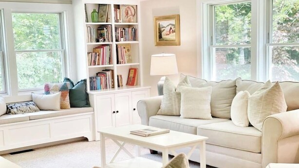 A cozy living room with a white sofa, a coffee table, and a bookshelf filled with books. - Serene & Cozy 3BR Home w/ Large Deck on River (Stowe)