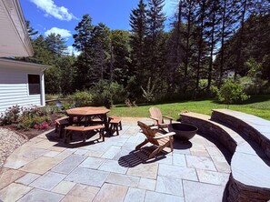 A patio with a wooden table and chairs, a fire pit, and a stone wall. - Clean, perfect home a mile from historic Waterbury (Waterbury Village Historic District)