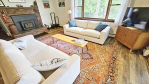 A living room with a fireplace, a sofa, a coffee table, and a TV. - Rustic Farmstay, Bucolic retreat w/Endless Views (Stowe)