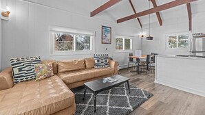 A spacious living room with a leather sofa, a coffee table, and a kitchen area with a white countertop and wooden beams. - New Stowe remodel, perfect location,many amenities (Stowe)