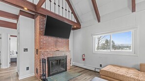A living room with a brick fireplace, a mounted TV, a large window with a view, and a leather sofa. - New Stowe remodel, perfect location,many amenities (Stowe)
