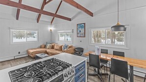 A kitchen with a gas stove, a dining table with chairs, a sofa, and large windows. - New Stowe remodel, perfect location,many amenities (Stowe)