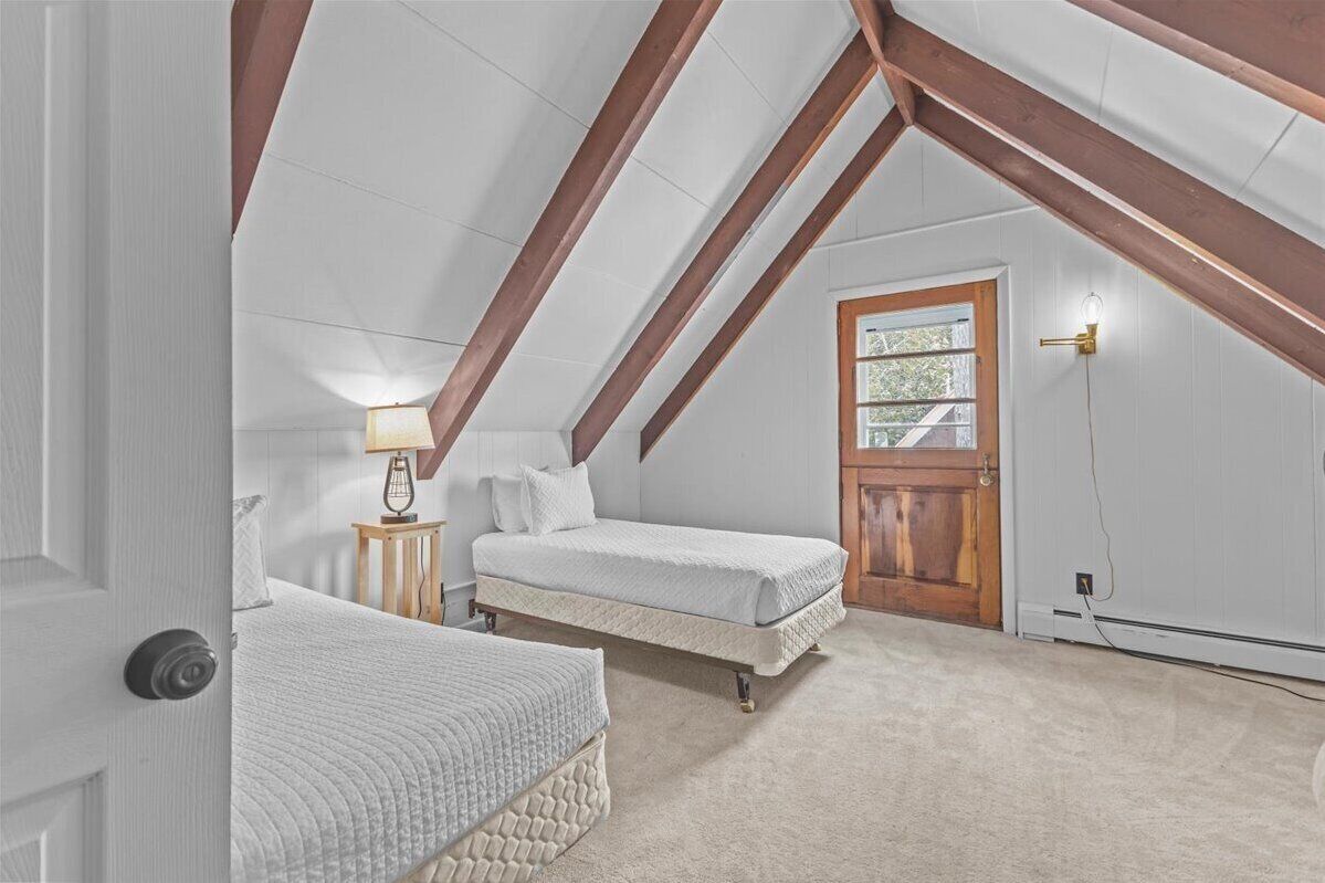 A bedroom with two beds, a wooden door, and a sloped ceiling with exposed beams.