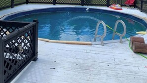 En swimmingpool med ett svart staket, ett trädäck och en stege som leder ner i vattnet.