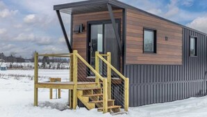 A modern, single-story cabin with a wooden exterior and a metal roof. It features a set of wooden stairs leading to a door, and a small porch area.