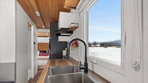 A modern kitchen with a wooden countertop, stainless steel sink, and a window overlooking a snowy landscape.