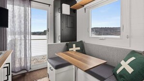 A compact RV interior with a kitchenette, a dining area, and a window offering a view of a snowy landscape.