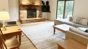 A living room with a fireplace, a sofa, a coffee table, and a TV mounted on the wall. - Large house heart of Stowe, amazing river for kids (Stowe)