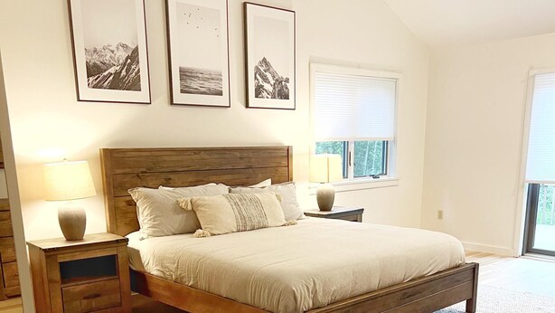 A bedroom with a wooden bed, a beige rug, wooden nightstands, and framed pictures on the wall. - Large house heart of Stowe, amazing river for kids (Stowe)