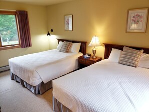 A hotel room with two single beds, a nightstand with a lamp, and a window with curtains. - Large house heart of Stowe, amazing river for kids (Stowe)