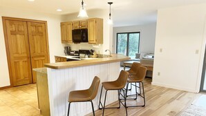 A modern kitchen with wooden cabinets, a black microwave, and a wooden island with bar stools. - Large house heart of Stowe, amazing river for kids (Stowe)