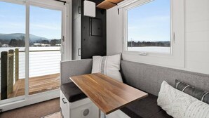 Un espacio habitable compacto con sofá, una mesita y vistas a un paisaje nevado a través de un ventanal corredero.