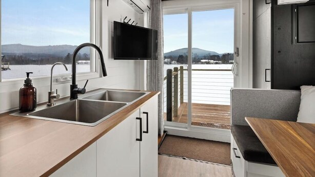 Cocina compacta con un lavamanos, un televisor montado sobre él y vistas a un paisaje nevado a través de una puerta corrediza.