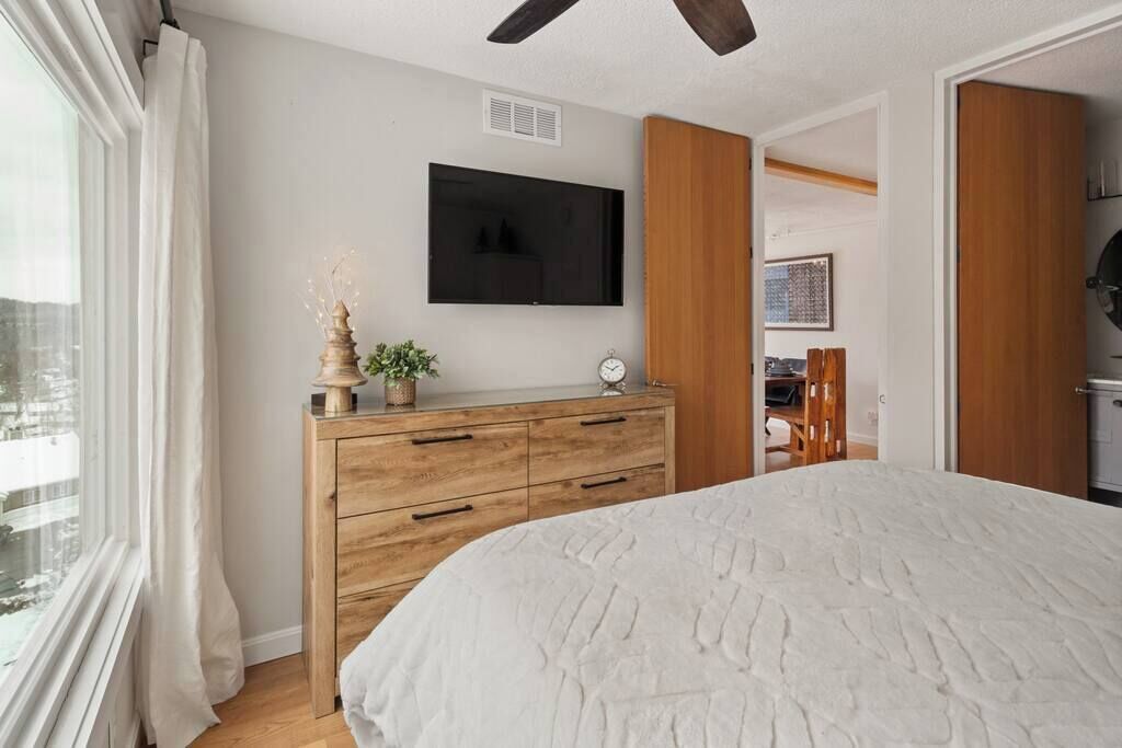 Een slaapkamer met een groot bed, een houten dressoir en een flatscreen televisie aan de muur.