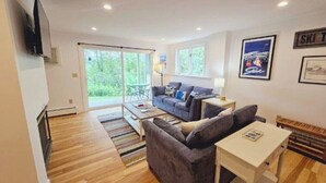 A modern living room with a sofa, a coffee table, and a TV mounted on the wall. - Cute two bedroom condo close to Stowe Mountain (Stowe)
