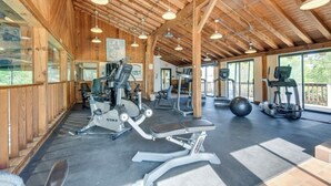 A gym with various exercise equipment, wooden beams on the ceiling, and large windows. - Cute two bedroom condo close to Stowe Mountain (Stowe)