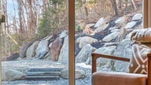 Ein Holztisch und ein Stuhl in einem Raum mit einem großen Fenster mit Blick auf eine felsige Landschaft und Bäume.