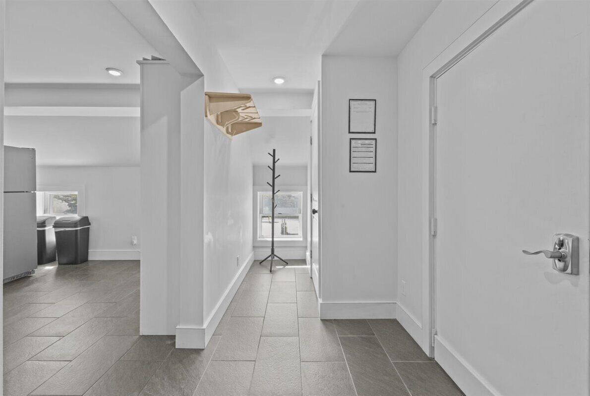 A modern hallway with a tiled floor, white walls, and a door on the right.