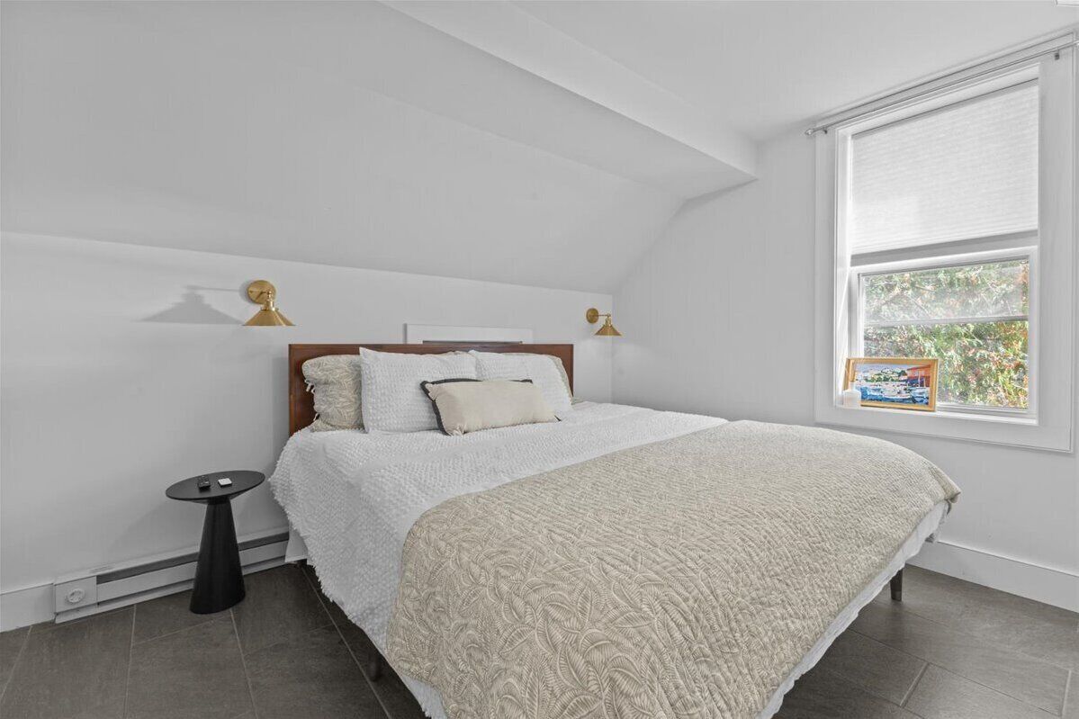 A bedroom with a bed, a small table, and a window with blinds.