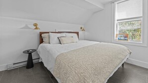 A bedroom with a bed, a small table, and a window with blinds.