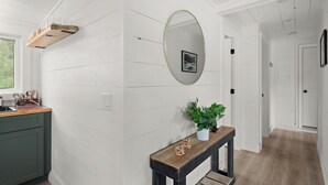Un couloir aux murs blancs, un banc en bois agrémenté d’une plante et un miroir.