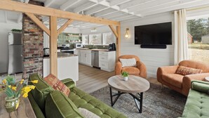 Une cuisine moderne avec des meubles blancs, un mur en briques et un plafond en bois. On y trouve un coin repas avec des canapés verts et une table ronde.