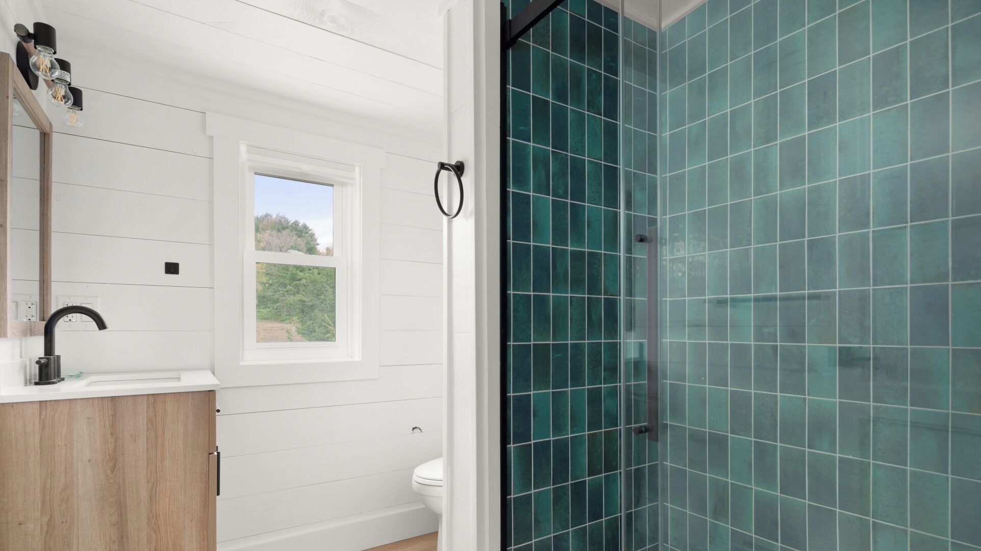 Une salle de bain avec un meuble-lavabo blanc, un robinet noir, une fenêtre et une douche aux carreaux de couleur turquoise.