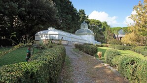 Une serre à structure en forme de dôme, entourée de haies bien entretenues et bordée d’un chemin de gravier.