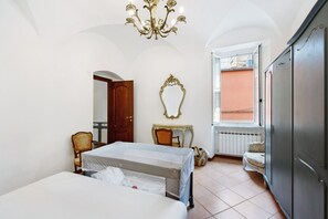 A bedroom with two beds, a chandelier, a mirror, a window with a view, and a wardrobe.