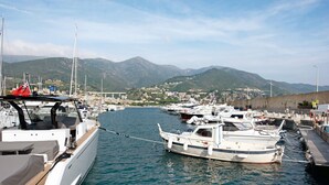 Un port de plaisance avec des bateaux amarrés, un paysage montagneux en arrière-plan et un ciel dégagé.