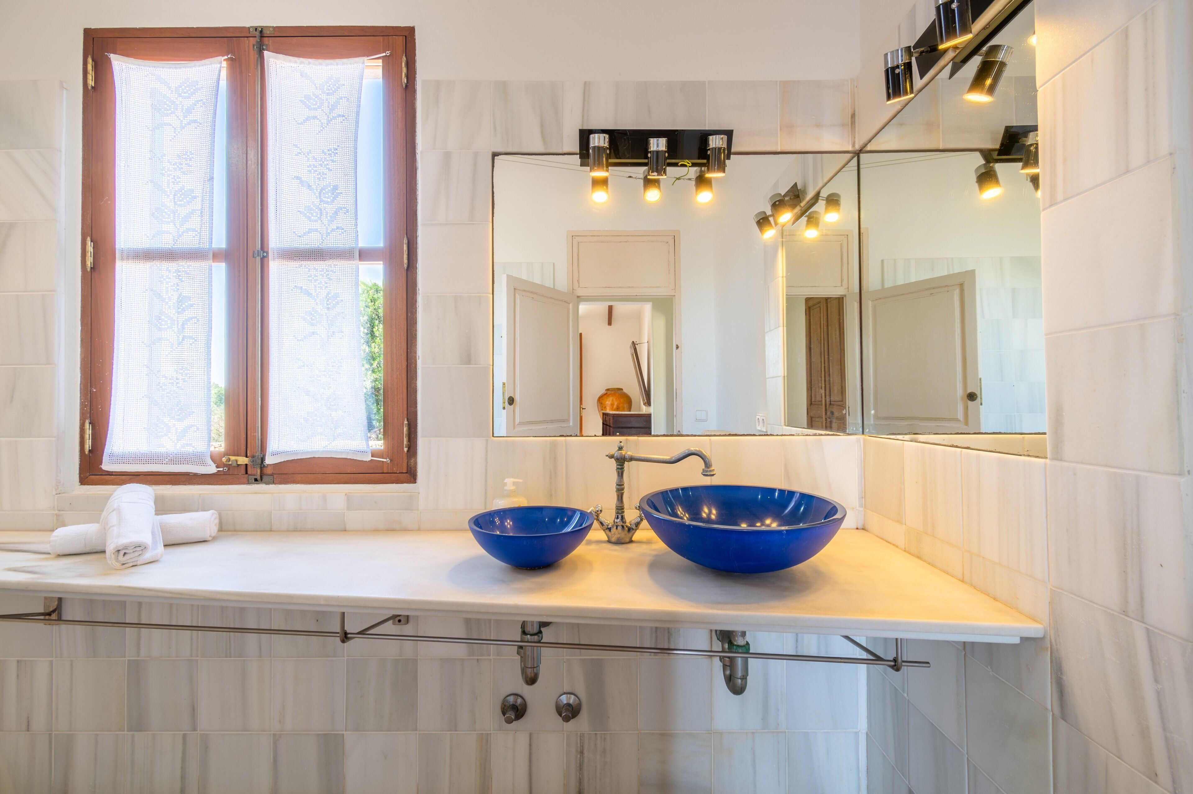 A bathroom with two blue sinks, a large mirror, and a window with lace curtains.