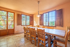 A spacious kitchen with a large wooden table and chairs, wooden cabinets, and large windows with shutters.