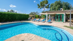 En swimmingpool med solstolar, en täckt uteplats och en byggnad med ett tak täckt av tegelpannor.