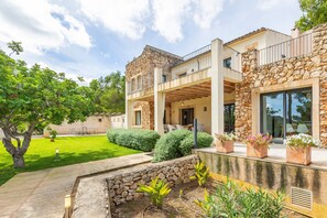 A modern two-story house with stone walls, a balcony, and a well-maintained garden.