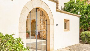 A building with a stone facade, a large arched entrance with glass doors, and a small window to the right. - Villa 'Pins' with Mountain View, Wi-Fi and Air Conditioning (Illes Balears)