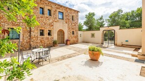 A stone building with a courtyard, outdoor seating, and a large planter. - Villa 'Pins' with Mountain View, Wi-Fi and Air Conditioning (Illes Balears)