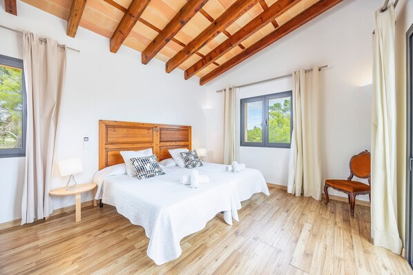 A bedroom with a wooden ceiling, two beds, a nightstand, a chair, and a window with curtains.