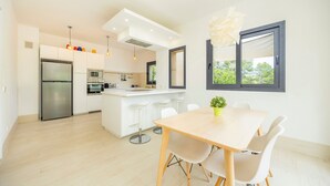 A modern kitchen with a central island, stainless steel appliances, and a dining area with a wooden table and white chairs. - Villa 'Pins' with Mountain View, Wi-Fi and Air Conditioning (Illes Balears)