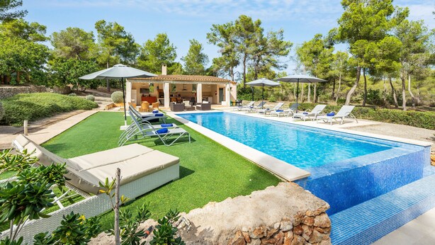 A swimming pool with lounge chairs and umbrellas, surrounded by greenery and a building with outdoor seating. - Villa 'Pins' with Mountain View, Wi-Fi and Air Conditioning (Illes Balears)