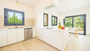 A modern kitchen with a dishwasher, a large window, and a dining area with a table and chairs. - Villa 'Pins' with Mountain View, Wi-Fi and Air Conditioning (Illes Balears)