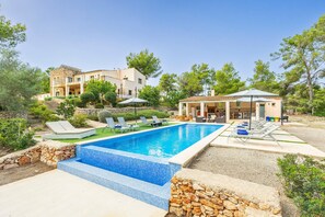 A swimming pool with lounge chairs, a stone wall, and a building with a tiled roof.
