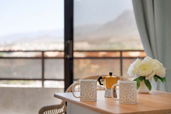 A table with two patterned mugs, a coffee pot, and a vase of flowers.